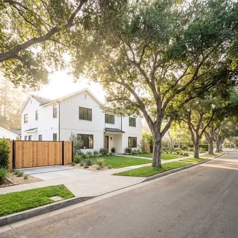 White two-story house behind a wood gate on a tree-lined street