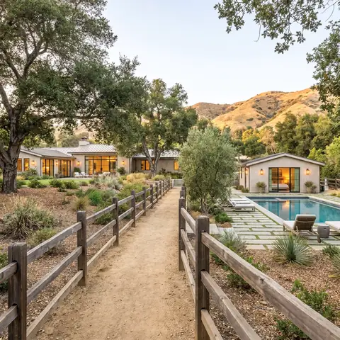 Ranch homes along a split-rail fence path with a pool under oak trees