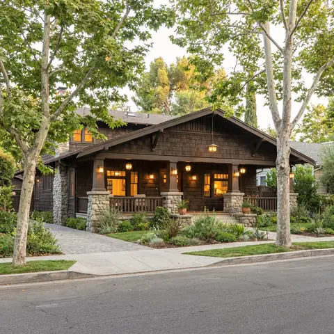 Craftsman bungalow with a deep front porch under sycamore trees at dusk