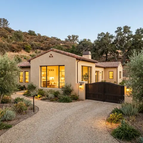 Stucco ranch house with a wood gate and a gravel drive in the hills