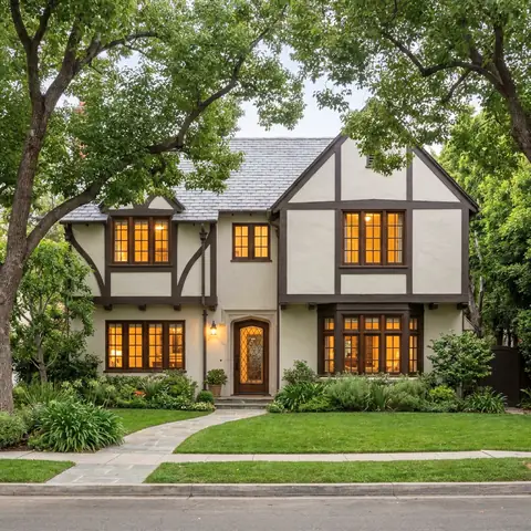Two-story Tudor-style house with dark trim under tall trees