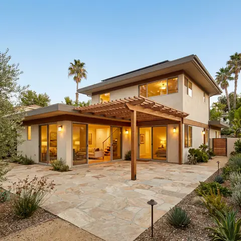 Two-story stucco house with a wood pergola over a stone patio